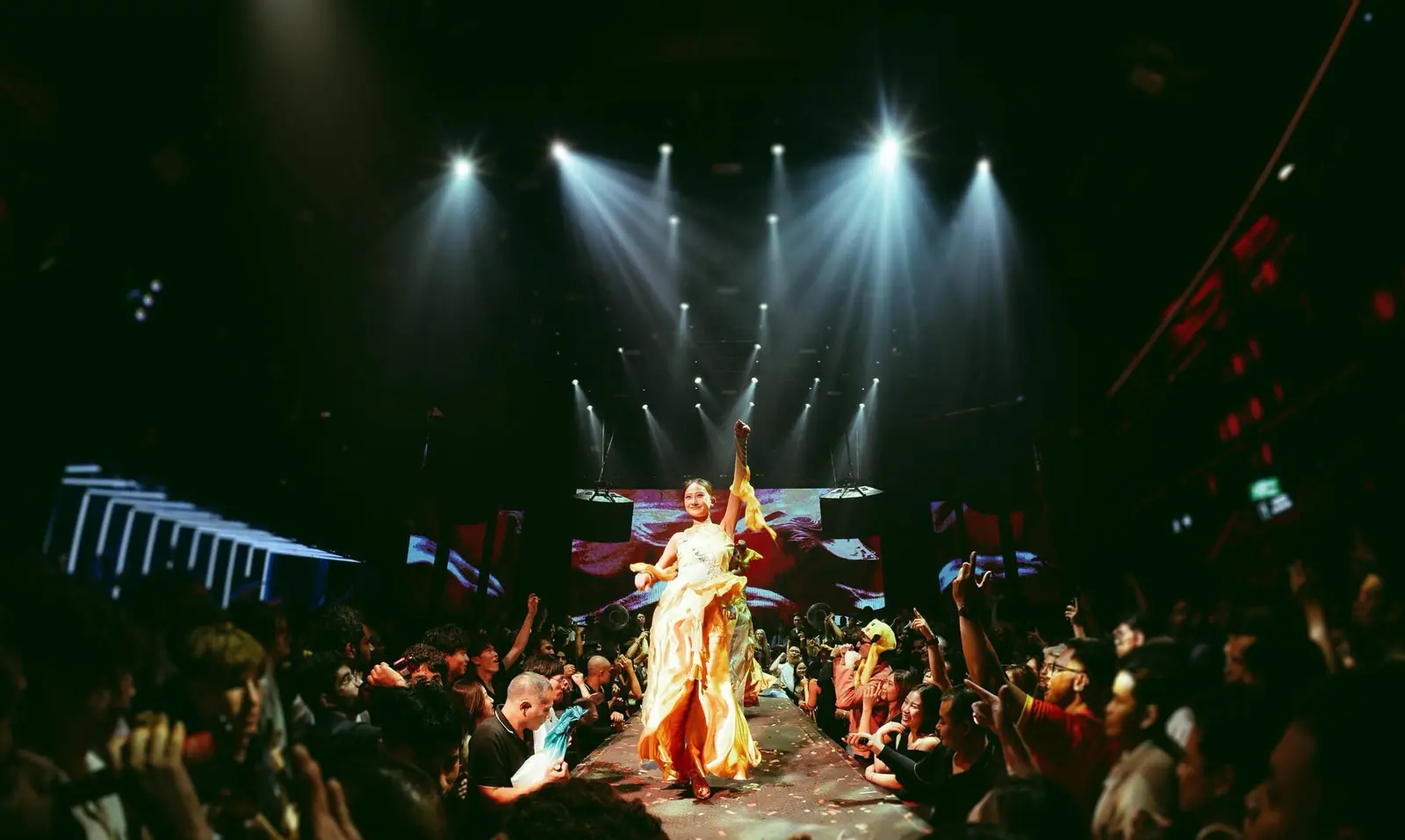Nghệ sĩ trong trang phục lụa vàng trình diễn trên đường catwalk giữa khán giả tại 1900 Le Théâtre